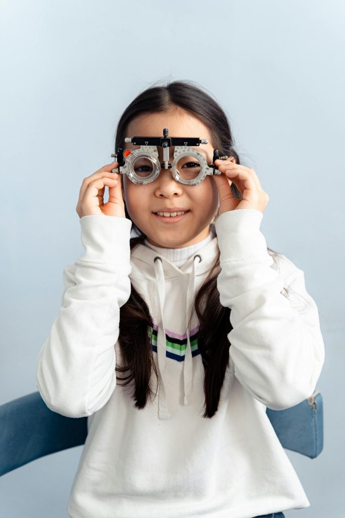 A young girl smiling while wearing an eye testing frame during a vision screening.